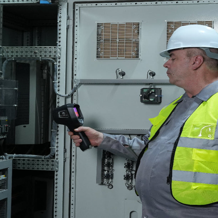 Electrician using a handheld thermal imager to inspect electrical wires for overheating.